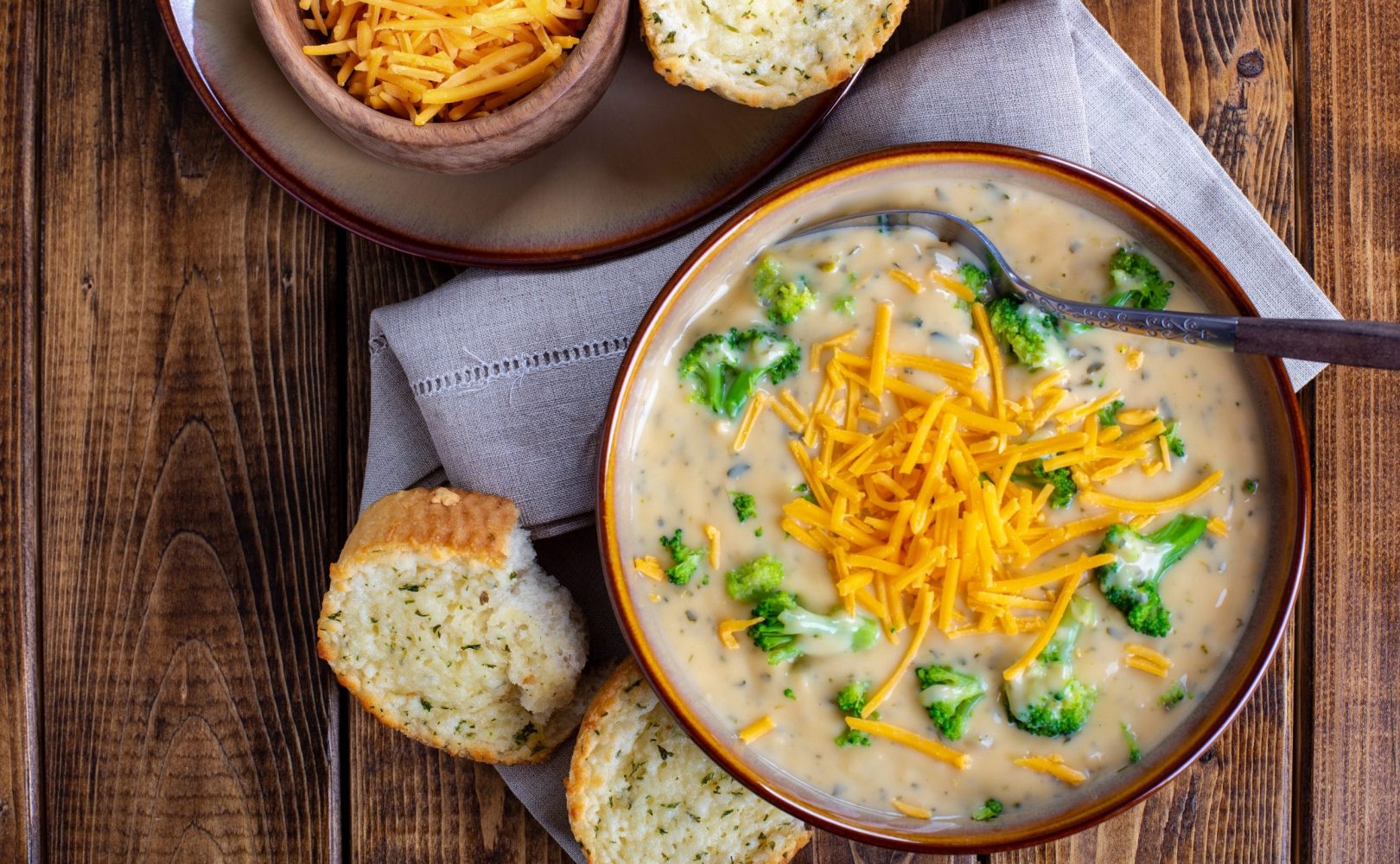 Overhead view of a bowl of creamy broccoli cheddar soup with toasted cheese bread on a wooden table